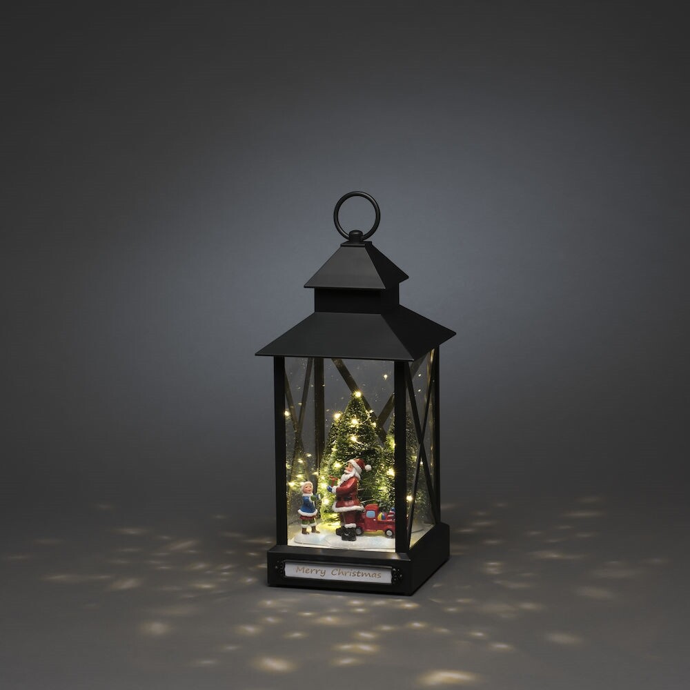 Bild zeigt eine charmante, kleine Laterne der Marke Konstsmide mit warmweißer LED-Beleuchtung, schwarz und batteriebetrieben. Das Motiv stellt einen Weihnachtsmann mit Kind und Weihnachtsbaum vor